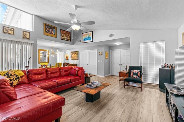 living room with vaulted ceiling, ceiling fan with notable chandelier, light hardwood / wood-style floors, and a textured ceiling