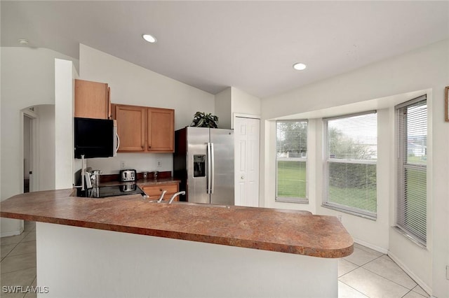 kitchen with lofted ceiling, brown cabinets, appliances with stainless steel finishes, a peninsula, and light tile patterned flooring