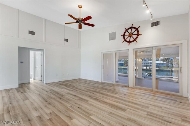 unfurnished living room with a high ceiling, rail lighting, light wood-type flooring, and ceiling fan