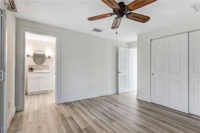 unfurnished bedroom featuring ensuite bath, a closet, ceiling fan, and light wood-type flooring