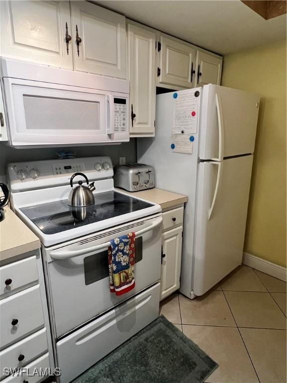 kitchen featuring light countertops, white appliances, light tile patterned flooring, and white cabinetry