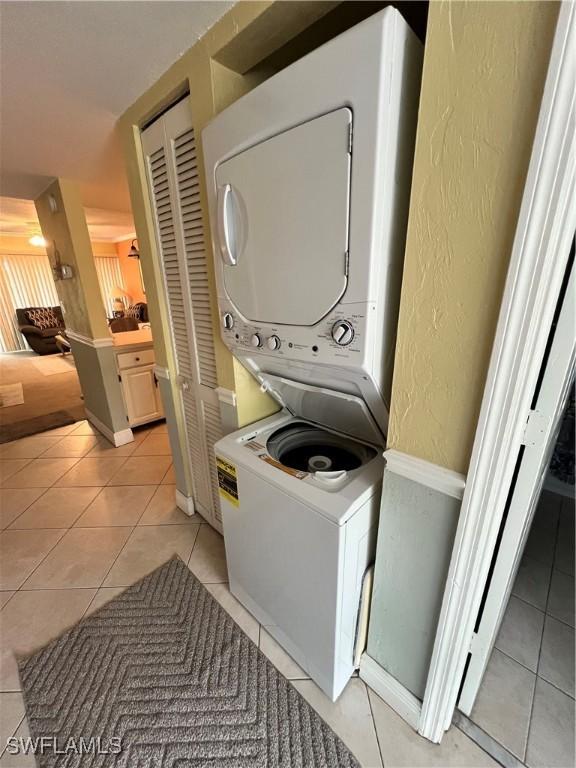 washroom featuring stacked washing maching and dryer, light tile patterned floors, laundry area, and a textured wall