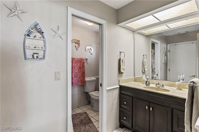 full bath with tile walls, toilet, wainscoting, vanity, and tile patterned flooring