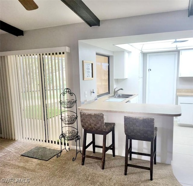 kitchen featuring a sink, white cabinets, light countertops, beamed ceiling, and a kitchen bar