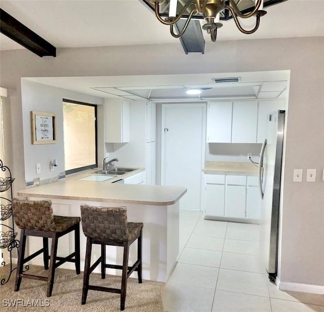 kitchen featuring light tile patterned floors, a peninsula, a sink, light countertops, and freestanding refrigerator