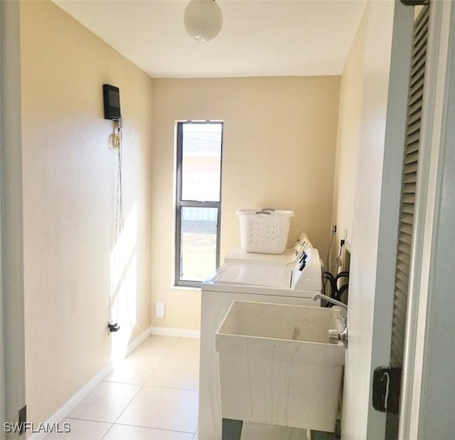 clothes washing area featuring light tile patterned floors, laundry area, separate washer and dryer, a sink, and baseboards