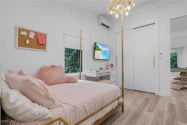 bedroom featuring an AC wall unit, a chandelier, light wood-type flooring, and a closet