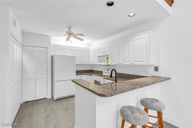 kitchen featuring white appliances, kitchen peninsula, white cabinets, and a breakfast bar