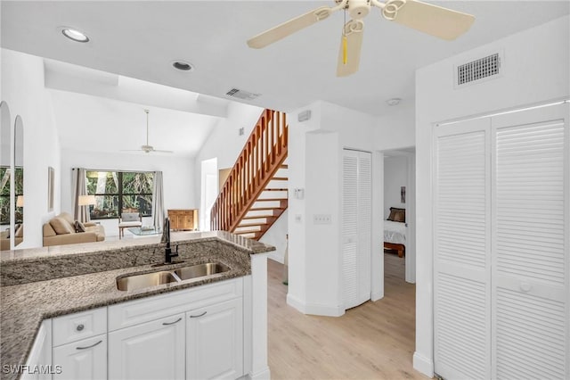 kitchen featuring sink, vaulted ceiling, light wood-type flooring, dark stone countertops, and white cabinets