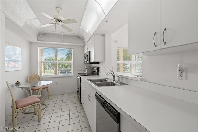 kitchen with light tile patterned floors, white cabinets, appliances with stainless steel finishes, a tray ceiling, and a sink