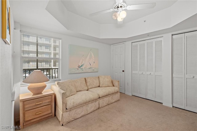 living area featuring ceiling fan, a tray ceiling, and carpet flooring