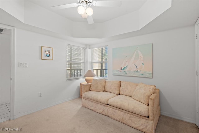 living room featuring carpet floors, a raised ceiling, ceiling fan, and baseboards