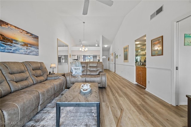 living room with ceiling fan with notable chandelier, high vaulted ceiling, and light hardwood / wood-style flooring