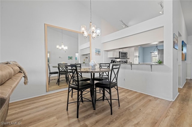 dining space featuring high vaulted ceiling, rail lighting, a chandelier, and light wood-type flooring