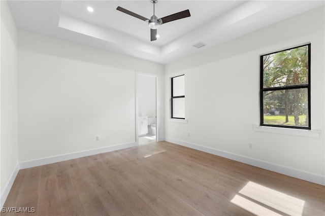 empty room featuring a raised ceiling, ceiling fan, and light hardwood / wood-style flooring