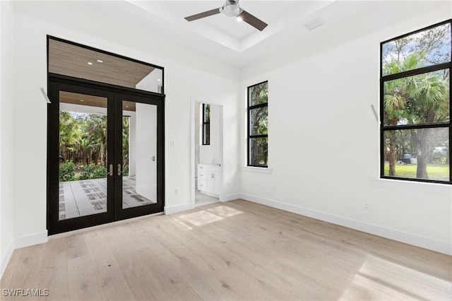 unfurnished room with ceiling fan, light hardwood / wood-style flooring, french doors, and a raised ceiling