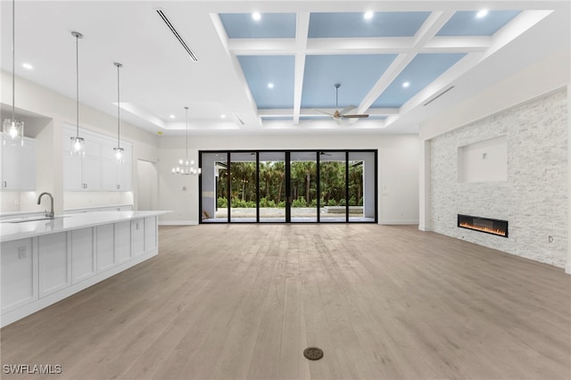 unfurnished living room featuring coffered ceiling, sink, ceiling fan with notable chandelier, a fireplace, and light hardwood / wood-style floors