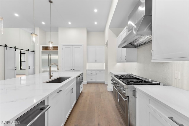 kitchen featuring white cabinetry, premium appliances, a barn door, and wall chimney exhaust hood