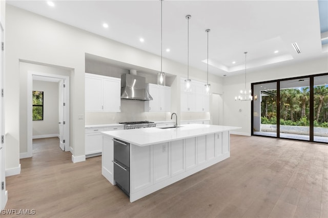 kitchen with white cabinetry, a kitchen island with sink, and wall chimney range hood