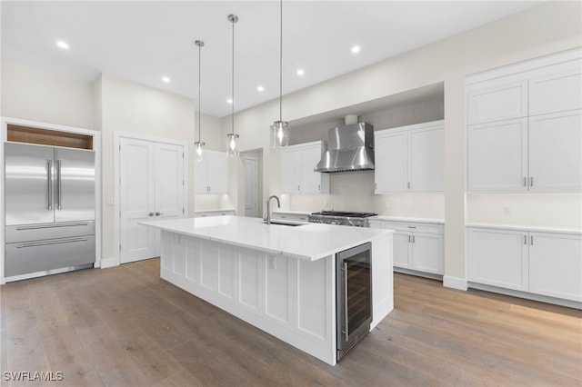 740 13th St NW, Naples, FL 34120 - kitchen featuring wall chimney exhaust hood, built in fridge, wine cooler, wood finished floors, and white cabinetry