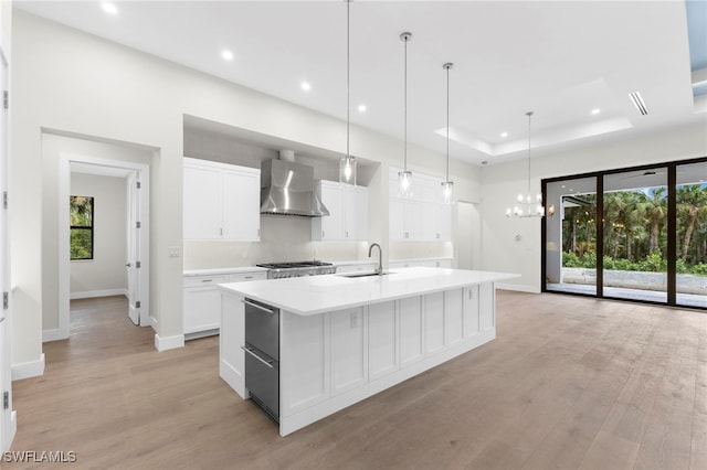740 13th St NW, Naples, FL 34120 - kitchen with wall chimney range hood, a large island, light wood-style floors, white cabinetry, and light countertops