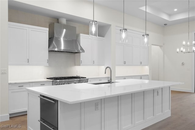 kitchen with an island with sink, white cabinets, and wall chimney exhaust hood