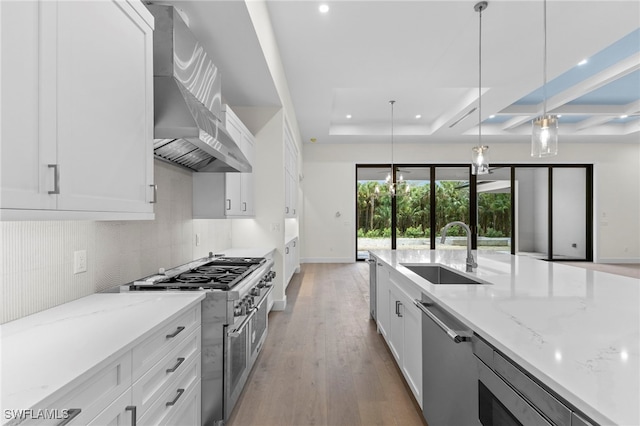 kitchen featuring decorative light fixtures, white cabinetry, sink, stainless steel appliances, and wall chimney range hood