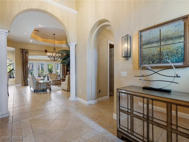 hallway featuring light tile patterned floors, a raised ceiling, a chandelier, and ornate columns