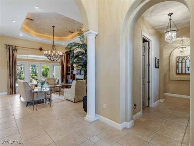 hallway with light tile patterned floors, a raised ceiling, a chandelier, and ornate columns