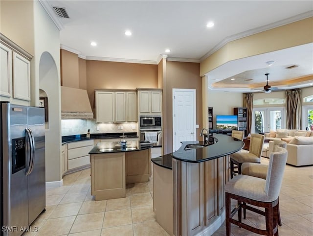 kitchen featuring an island with sink, sink, backsplash, stainless steel appliances, and cream cabinets