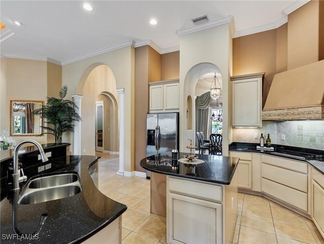 kitchen with sink, wall chimney range hood, dark stone countertops, a kitchen island, and light tile patterned flooring