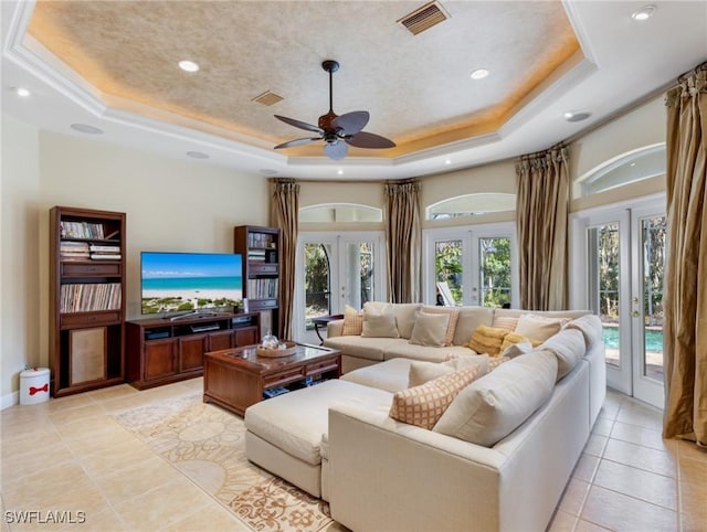 tiled living room with a tray ceiling, french doors, and ceiling fan