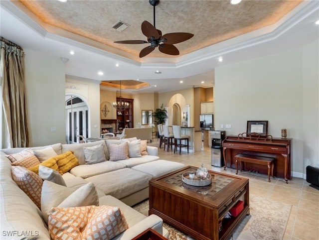 living room with a raised ceiling, light tile patterned flooring, a large fireplace, and ceiling fan