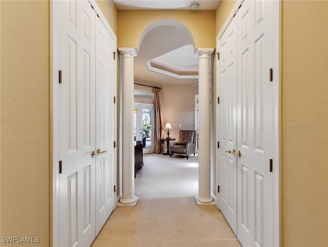 corridor with decorative columns, a raised ceiling, and light carpet