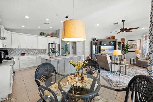 kitchen with light tile patterned floors, stainless steel refrigerator, white cabinetry, hanging light fixtures, and a center island with sink