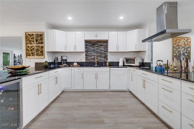 kitchen with wall chimney range hood, dishwasher, white cabinetry, beverage cooler, and dark stone counters