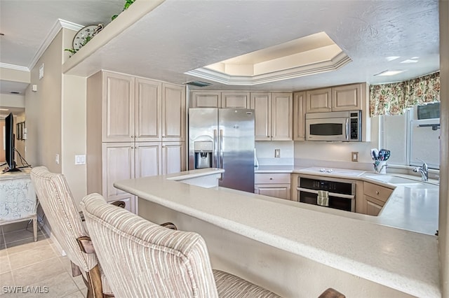 kitchen featuring light tile patterned floors, a breakfast bar, stainless steel appliances, ornamental molding, and a raised ceiling