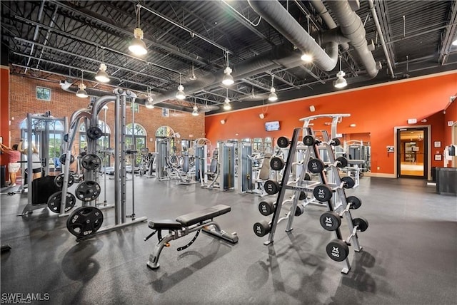 exercise room with a towering ceiling, track lighting, and brick wall