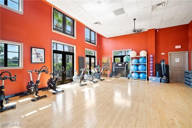 exercise room with french doors, a towering ceiling, a paneled ceiling, and hardwood / wood-style floors