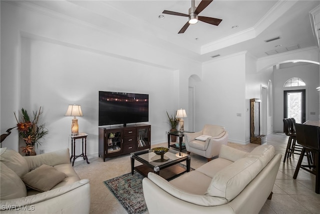 tiled living room with ceiling fan, ornamental molding, and a tray ceiling