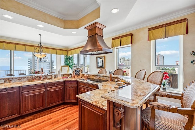 kitchen with pendant lighting, crown molding, black electric stovetop, a tray ceiling, and a kitchen bar