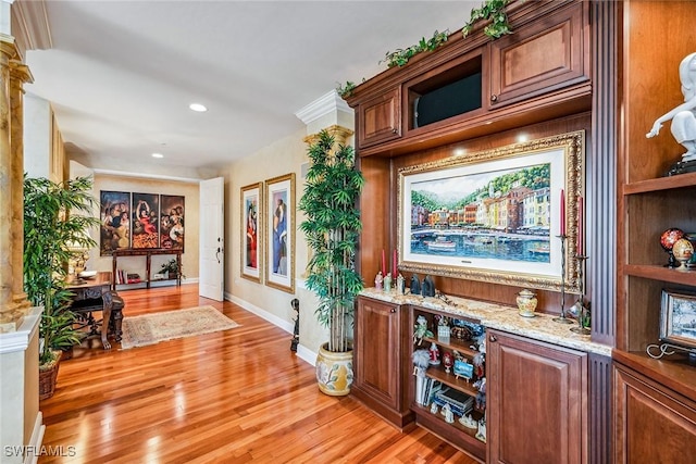 bar featuring decorative columns, light stone countertops, and light wood-type flooring