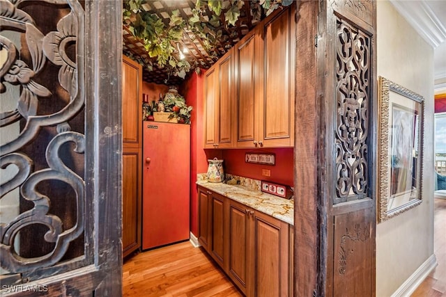 bar featuring light stone counters, ornamental molding, and light hardwood / wood-style floors