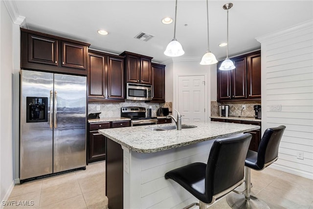 kitchen with light tile patterned flooring, hanging light fixtures, stainless steel appliances, light stone countertops, and a center island with sink