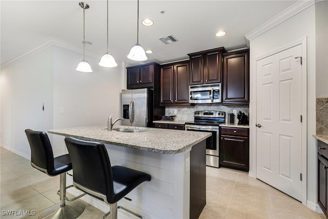 kitchen with sink, light tile patterned floors, appliances with stainless steel finishes, an island with sink, and decorative light fixtures