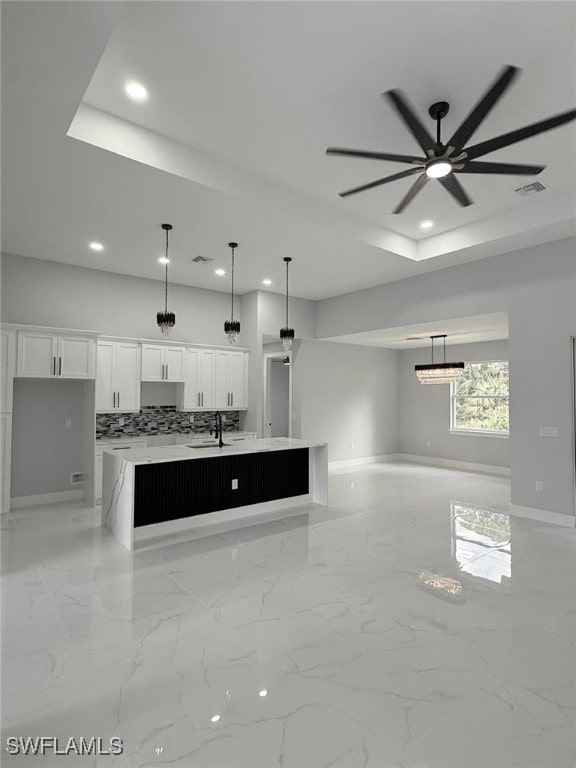 kitchen featuring a kitchen island with sink, pendant lighting, and white cabinets