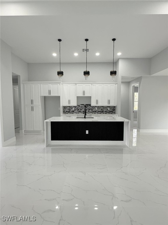 kitchen featuring sink, decorative light fixtures, white cabinets, a kitchen island with sink, and backsplash