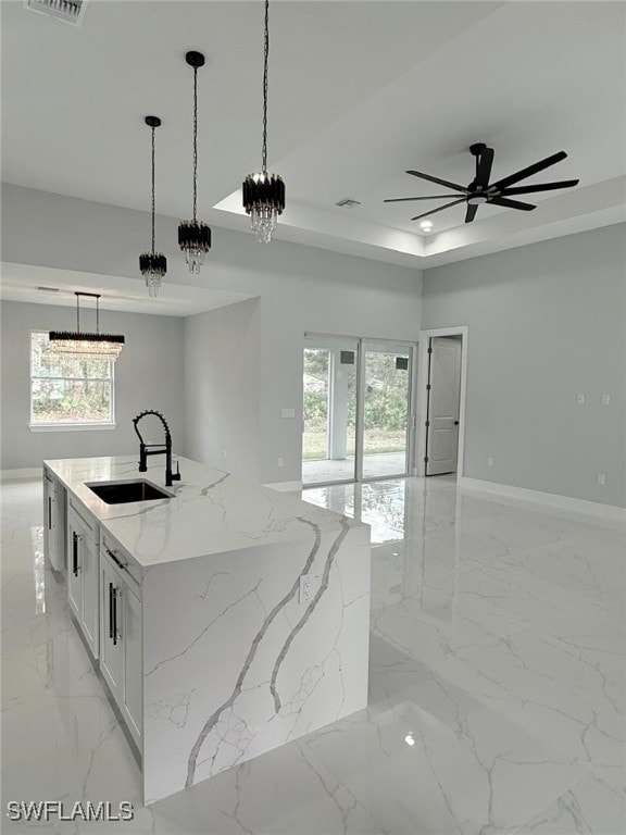 kitchen featuring sink, a center island with sink, pendant lighting, light stone countertops, and white cabinets