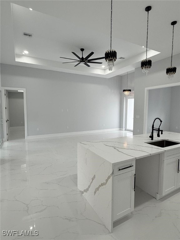 kitchen with sink, white cabinetry, light stone counters, hanging light fixtures, and a raised ceiling