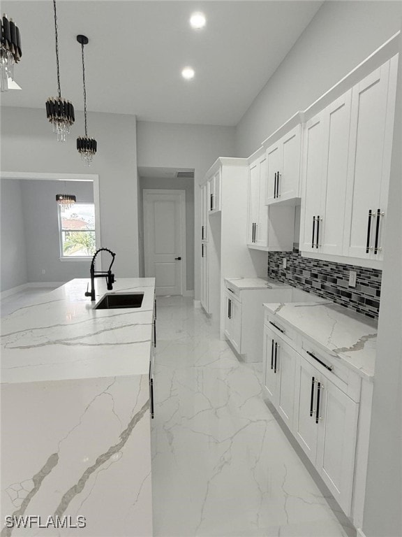 kitchen with tasteful backsplash, white cabinetry, sink, and light stone counters